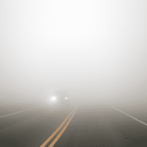 foggy road with car driving forward with headlights on to prevent accident in bad weather